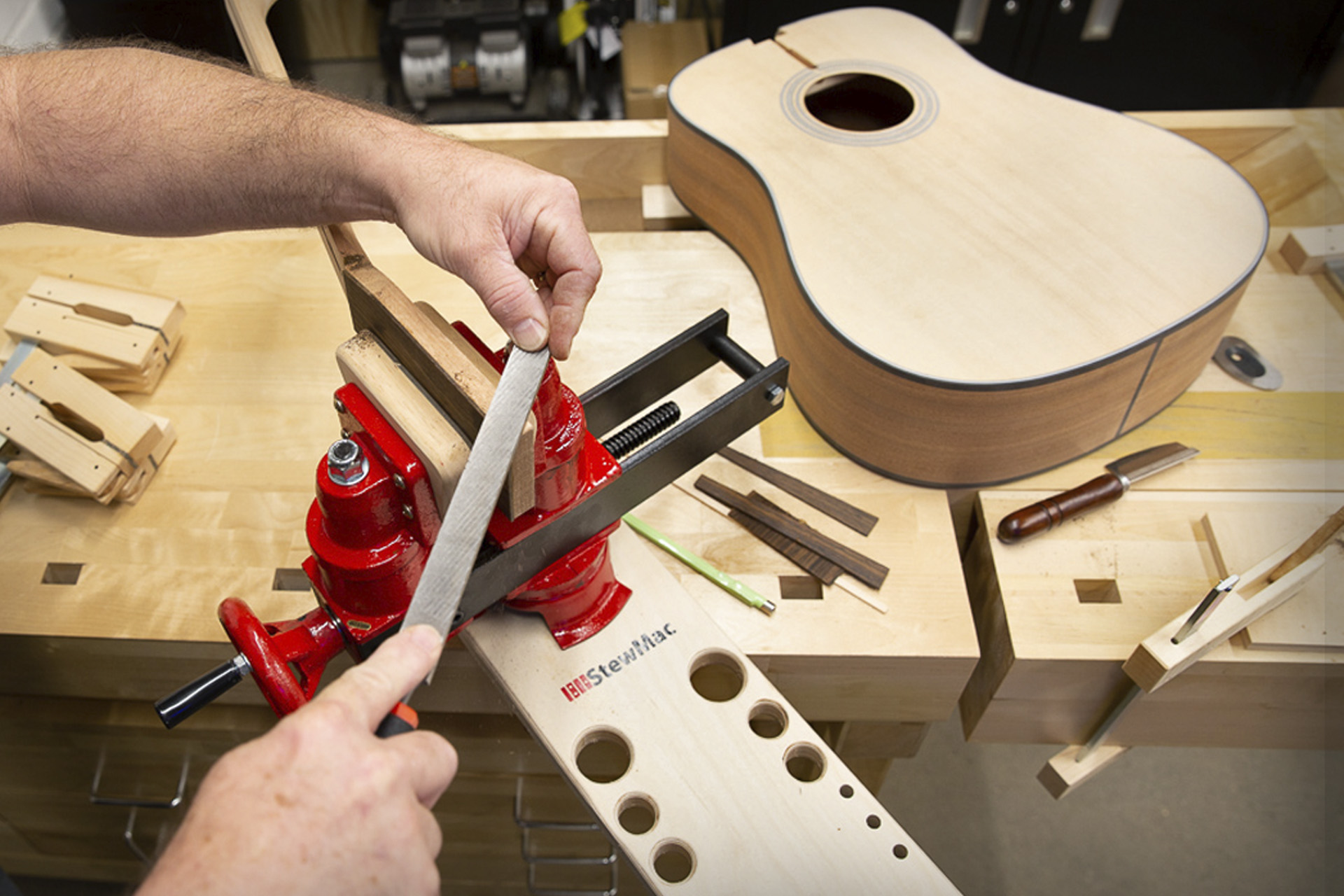 Acoustic guitar on bench with headstock being filed in vise