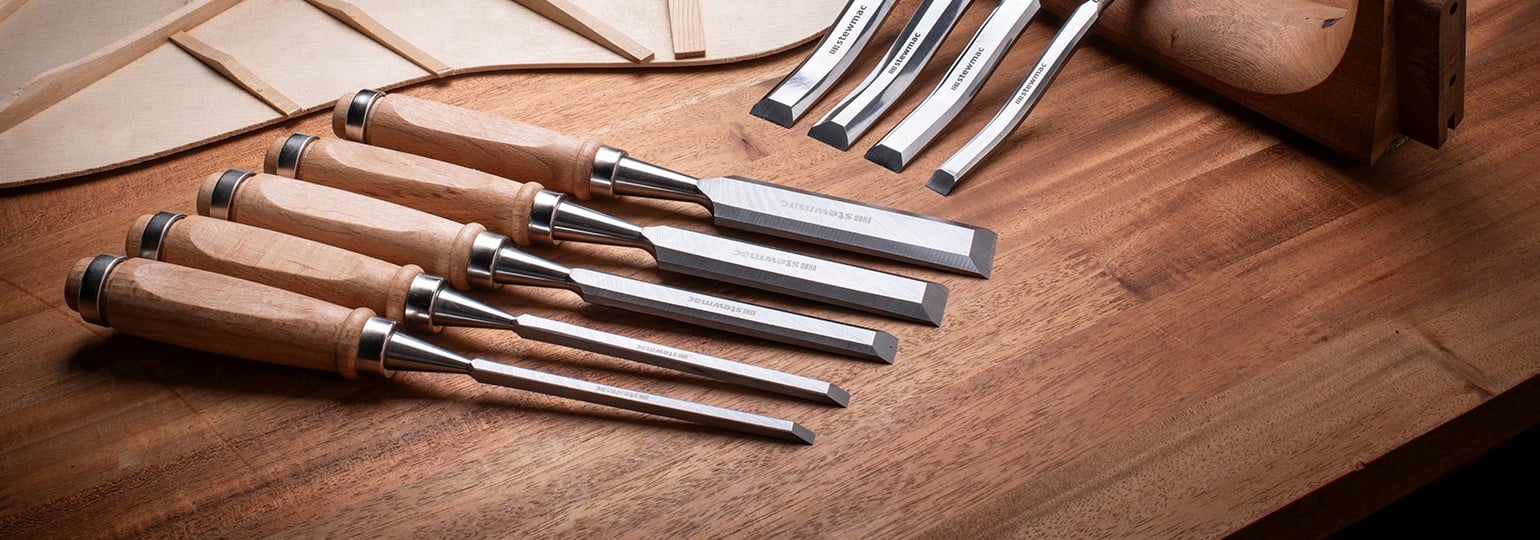 Set of wood chisels with acoustic guitar braces and neck on a bench.