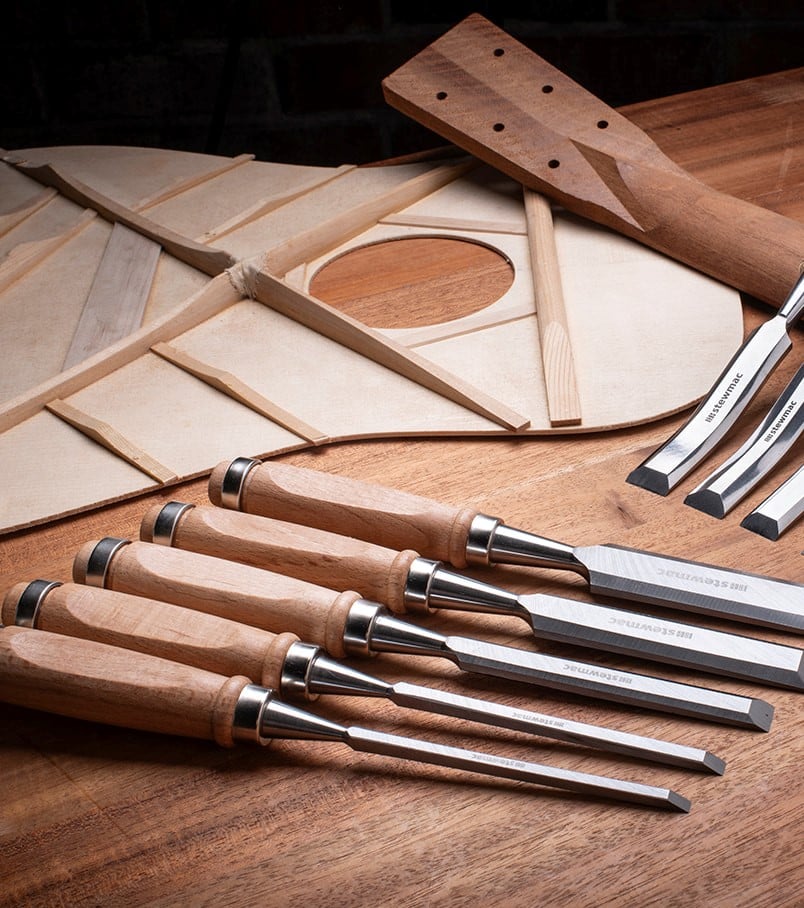 Set of wood chisels with acoustic guitar braces and neck on a bench.