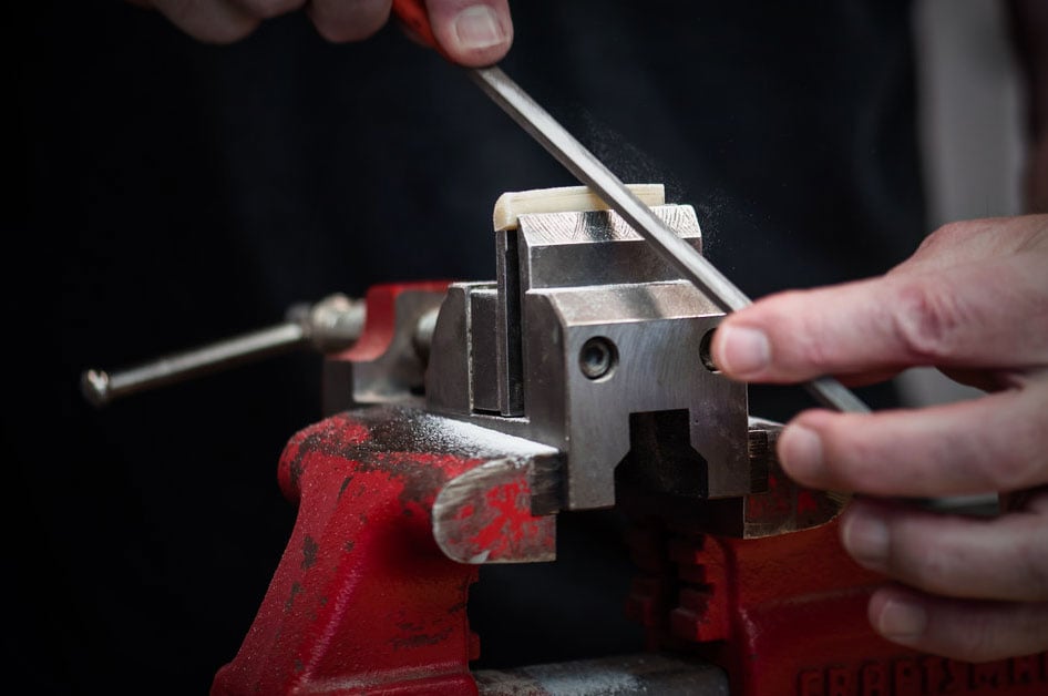 Hands using file to shape nut in vise