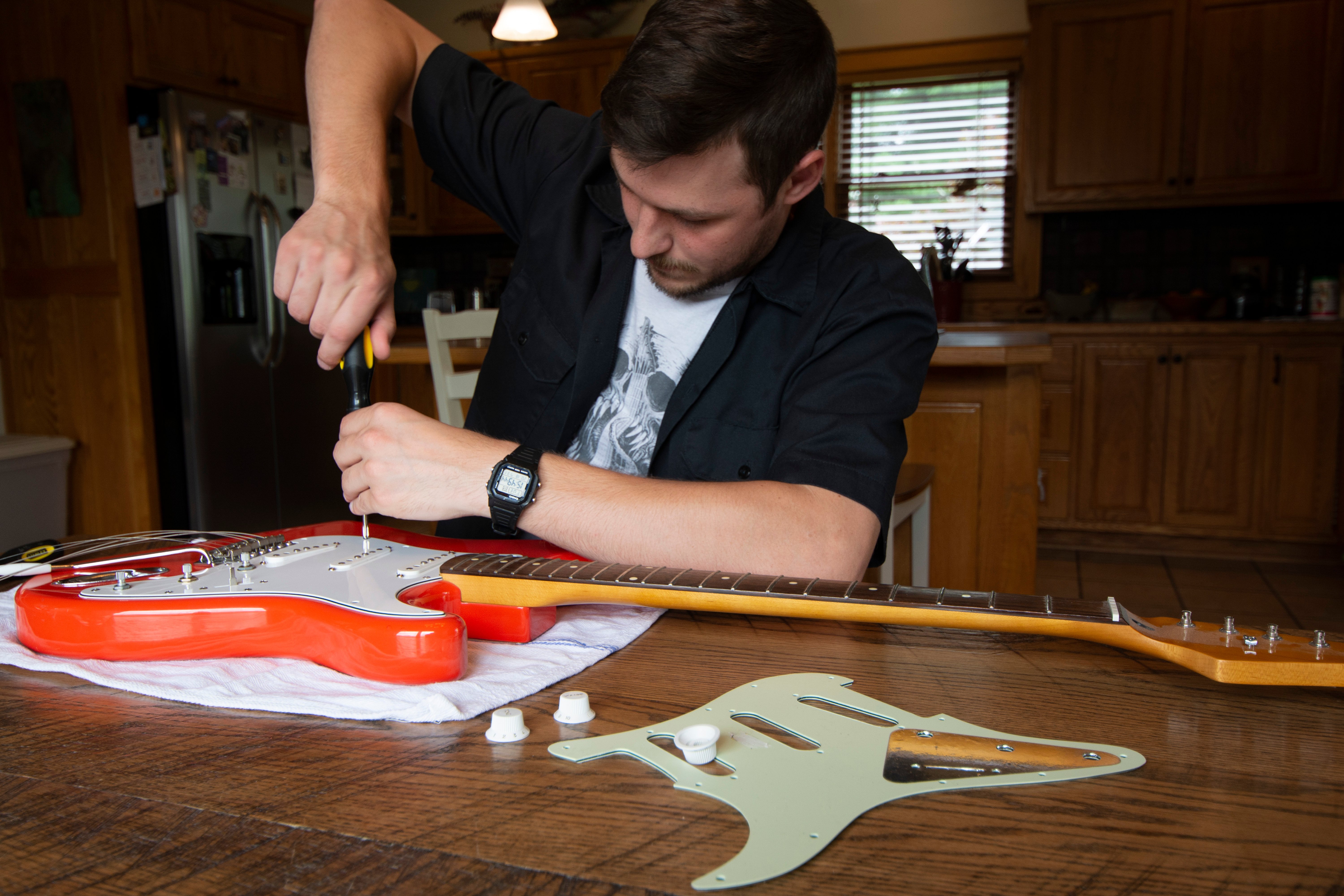 Man unscrewing and replacing pickguard on electric guitar