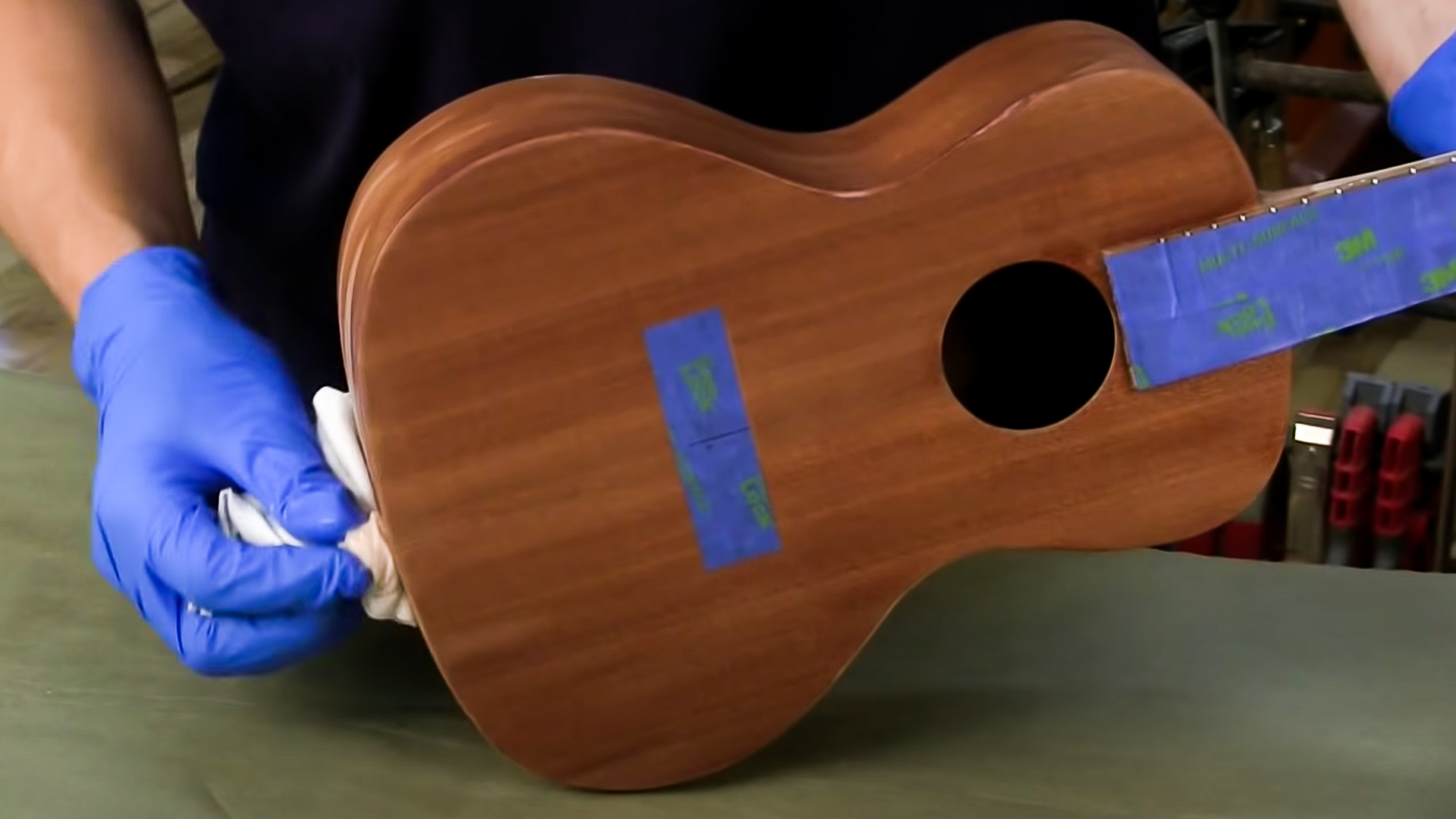 Hands wiping finish coat on ukulele body with rag